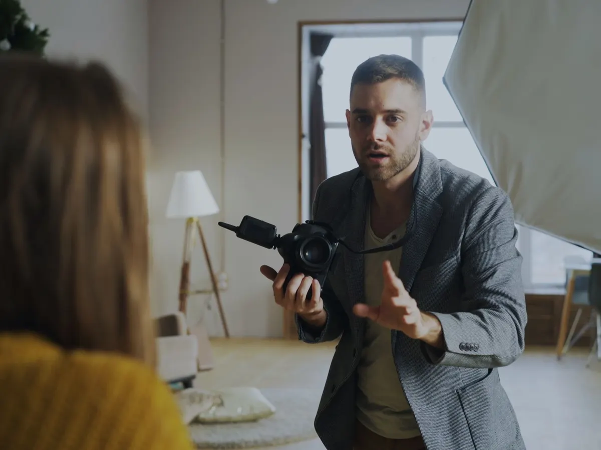 Ein Fotograf mit Kamera in der Hand spricht im Studio mit seiner Kundin, im Hintergrund ein Softbox-Licht.