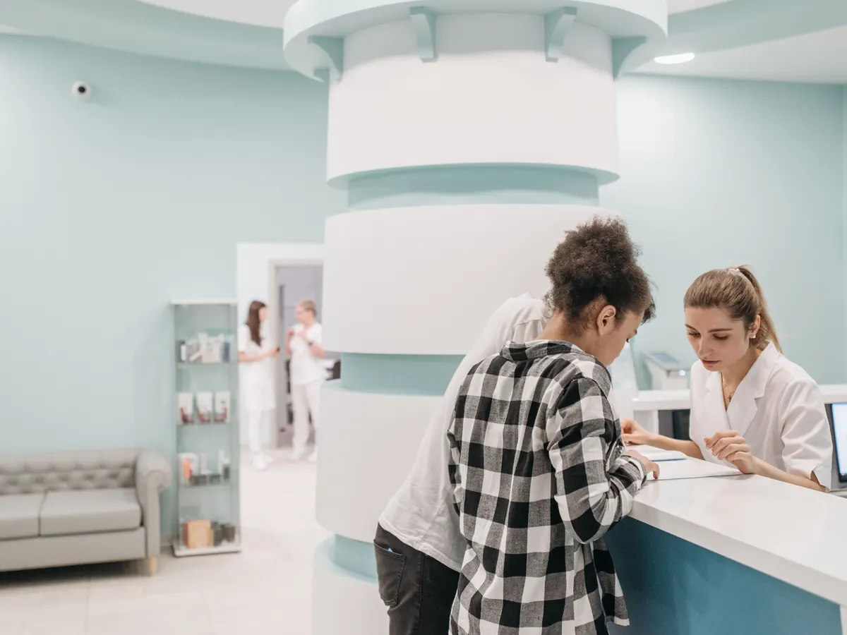 Eine Patientin steht am hellen Empfang einer Praxis und bespricht mit der Mitarbeiterin ein Formular.