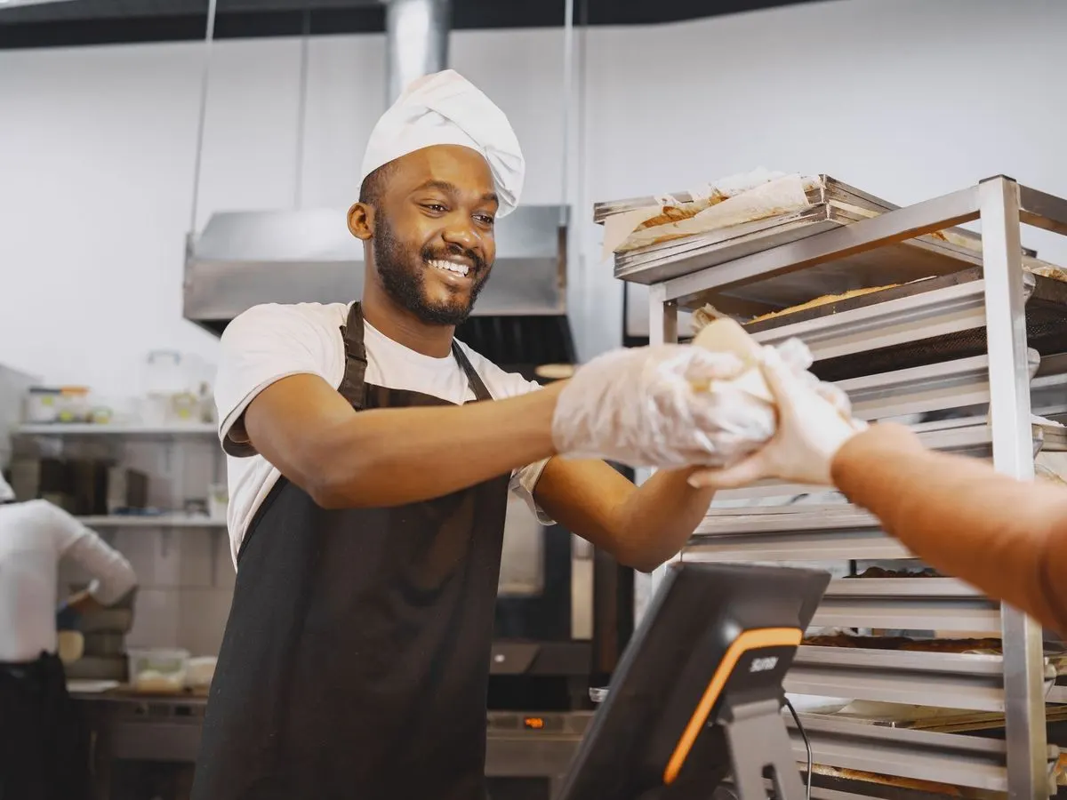 Ein Bäcker reicht einer Kundin über die Theke frisches Brot.