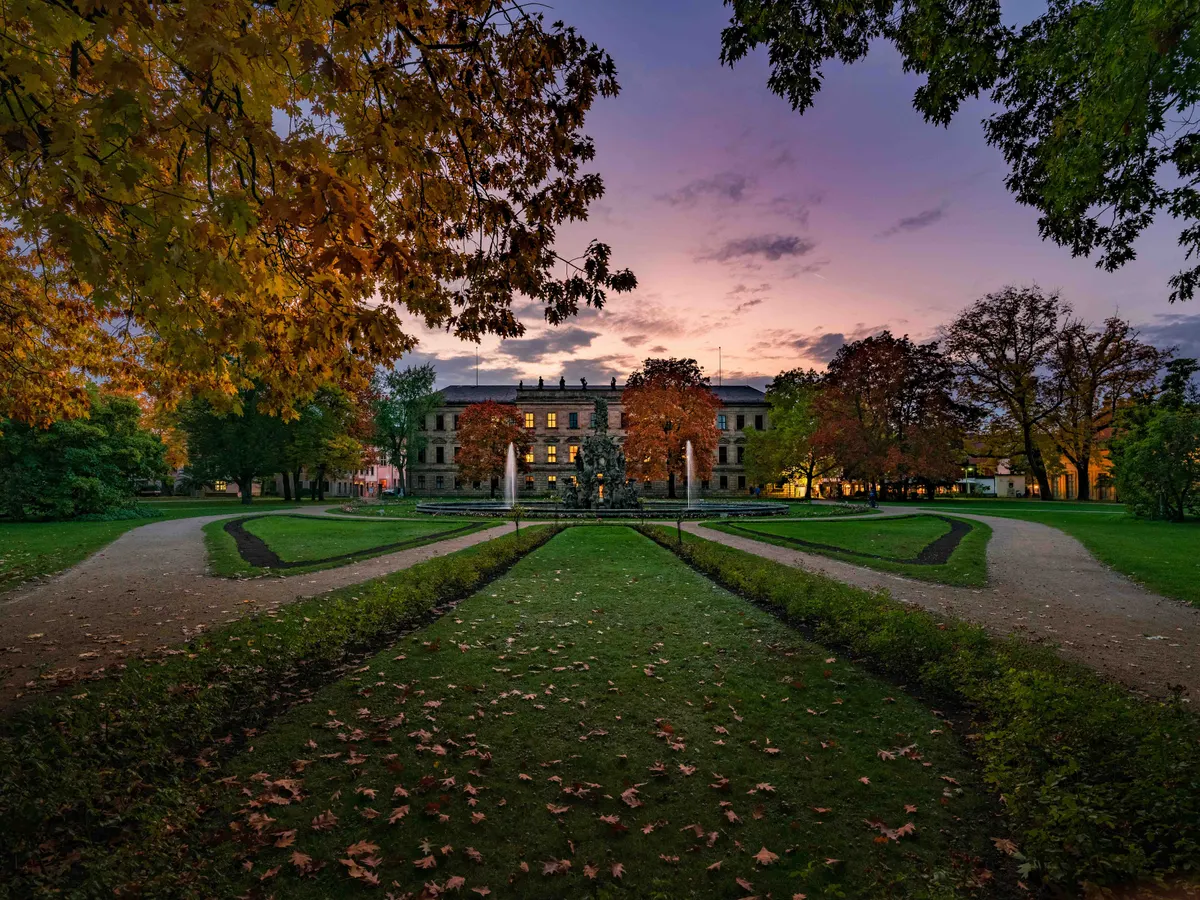 Der Erlanger Schlossgarten im Herbst bei Abenddämmerung, im Hintergrund das Schloss mit Brunnen.